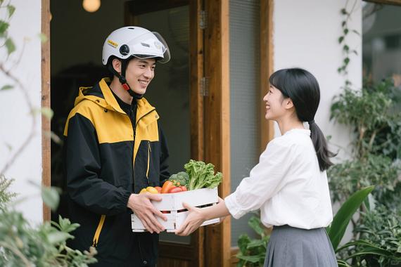 外卖员面带笑容为女士递送装有蔬菜的箱子